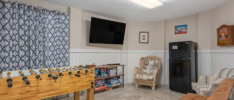 Un salon avec un baby-foot, une télévision, un réfrigérateur et un fauteuil à rayures.