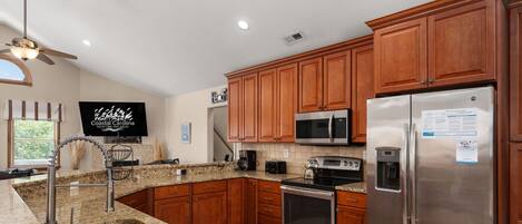 A modern kitchen with granite countertops, stainless steel appliances, wooden cabinets, and a built-in microwave.