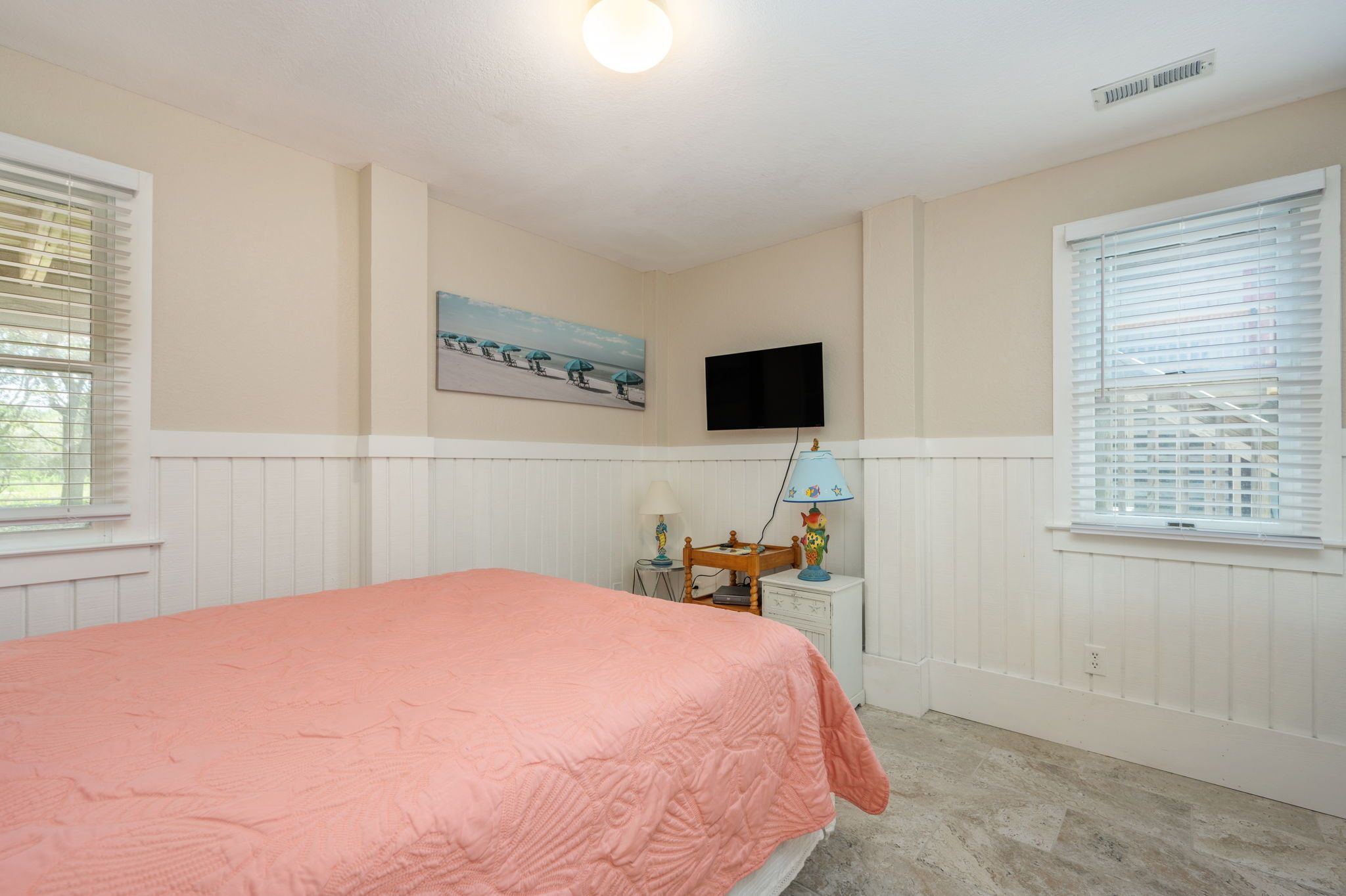 A bedroom with a bed, a television mounted on the wall, and a window with blinds.