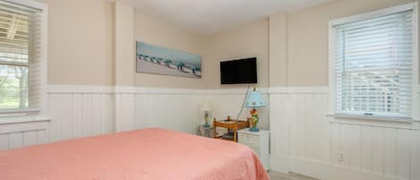 A bedroom with a bed, a television mounted on the wall, and a window with blinds.
