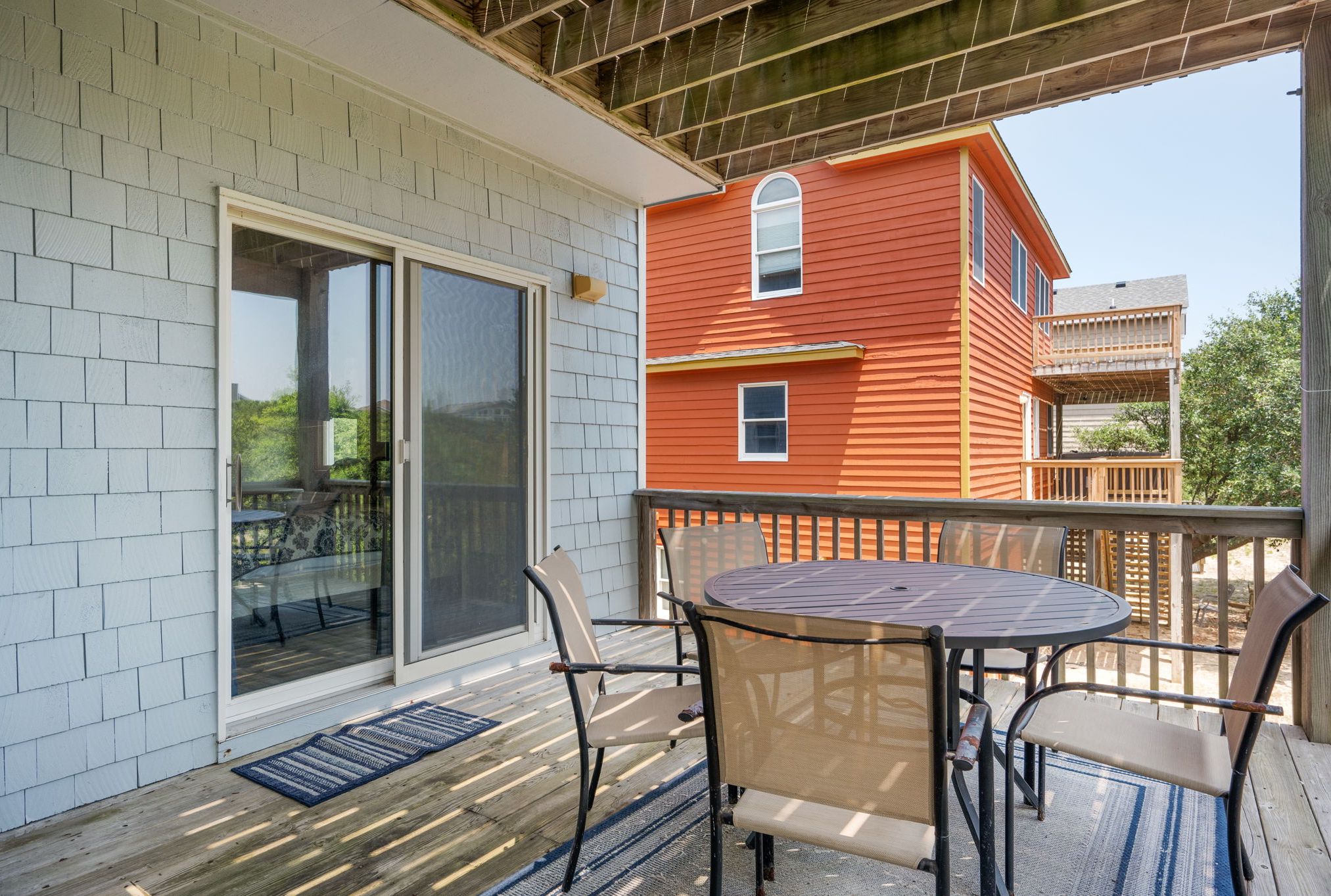 A covered patio with a table and chairs, a sliding glass door, and a red building in the background.