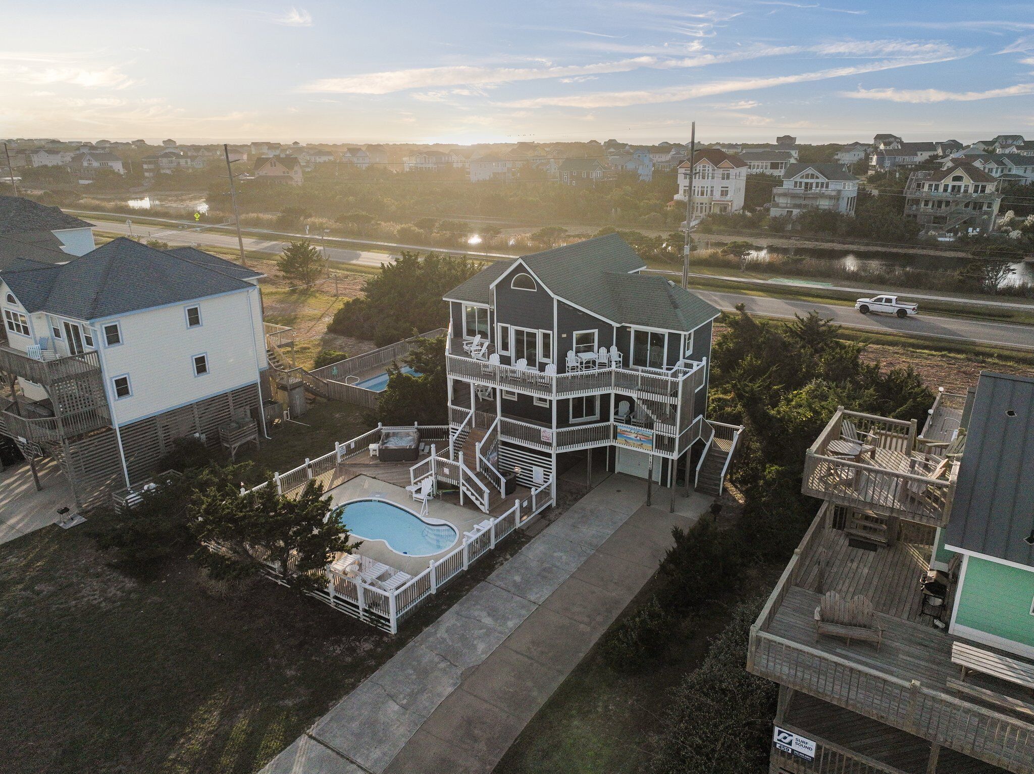 A large, multi-story house with a pool, surrounded by other houses.