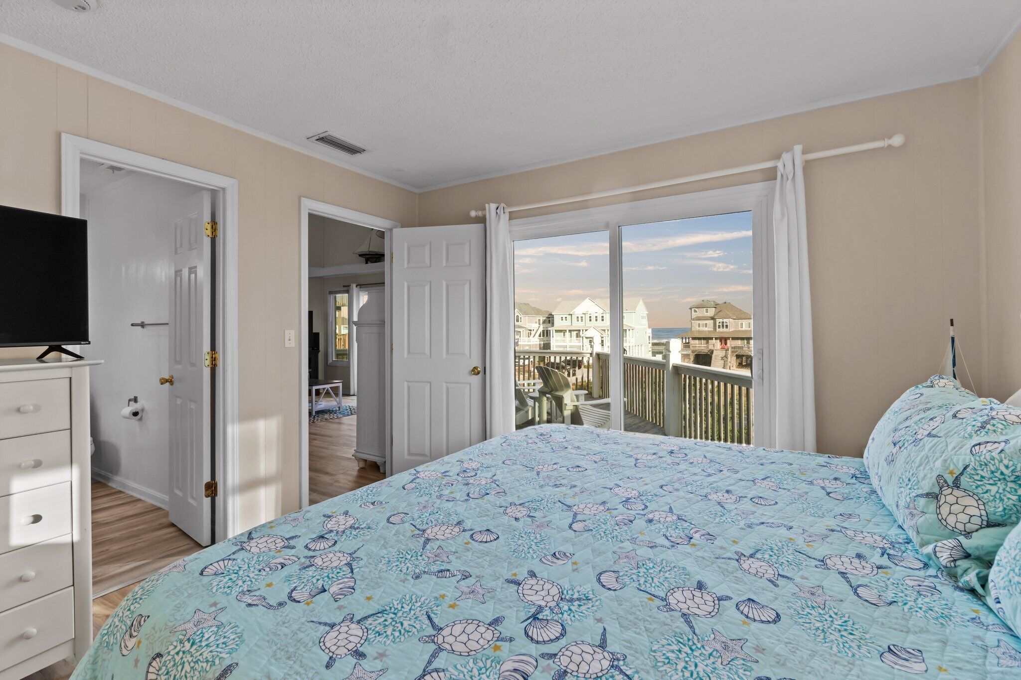 Une chambre avec un grand lit, un téléviseur posé sur une commode et un balcon offrant une vue sur les immebles.