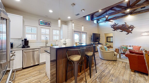 Una cocina moderna con barra, suelo de madera y una zona de estar con sofá y sillones.