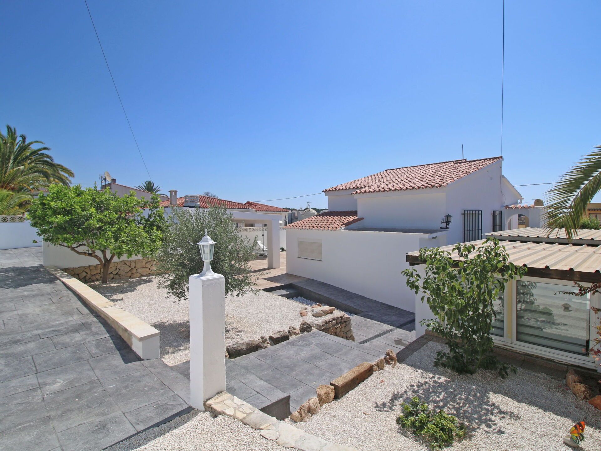 A residential area with a white house, a stone wall, and a small garden with gravel paths and a lamp post.