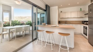A modern kitchen with a central island, bar stools, and a dining area with a view of the desert. - Jardines - Tajaste 2.4 NATURE RESERVE VIEW 2B (Arona)