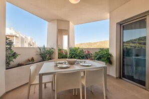 A balcony with a table set for two, surrounded by potted plants and overlooking a desert landscape.