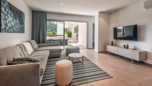 A modern living room with a sofa, ottoman, and a TV on a wall. - Jardines - Tajaste 2.4 NATURE RESERVE VIEW 2B (Arona)