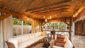Un espace extérieur aménagé avec des sièges, abrité par un toit de chaume, doté de mobilier en bois et de luminaires suspendus.