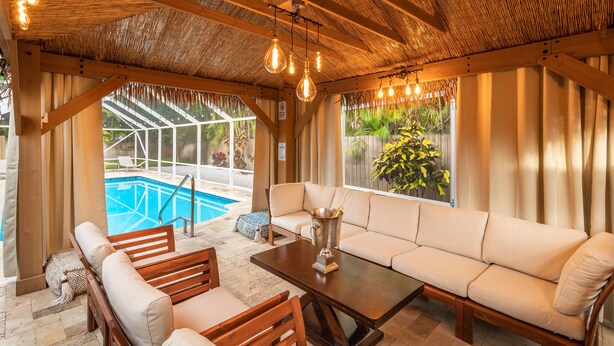 Un salon au bord de la piscine doté d’un plafond en bois, de luminaires suspendus, d’un canapé et d’une table.