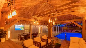 Un espace piscine intérieur aménagé avec du mobilier en bois et doté d’un toit de chaume.