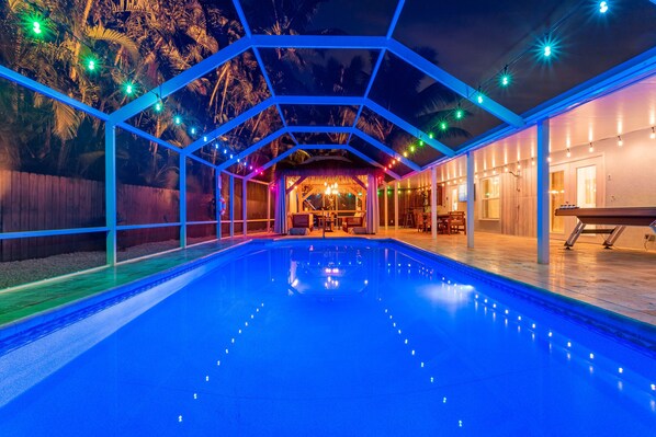 A swimming pool with a geometric glass enclosure, surrounded by palm trees and string lights.