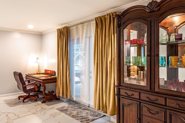 A room with a desk, chair, and a cabinet with glassware.