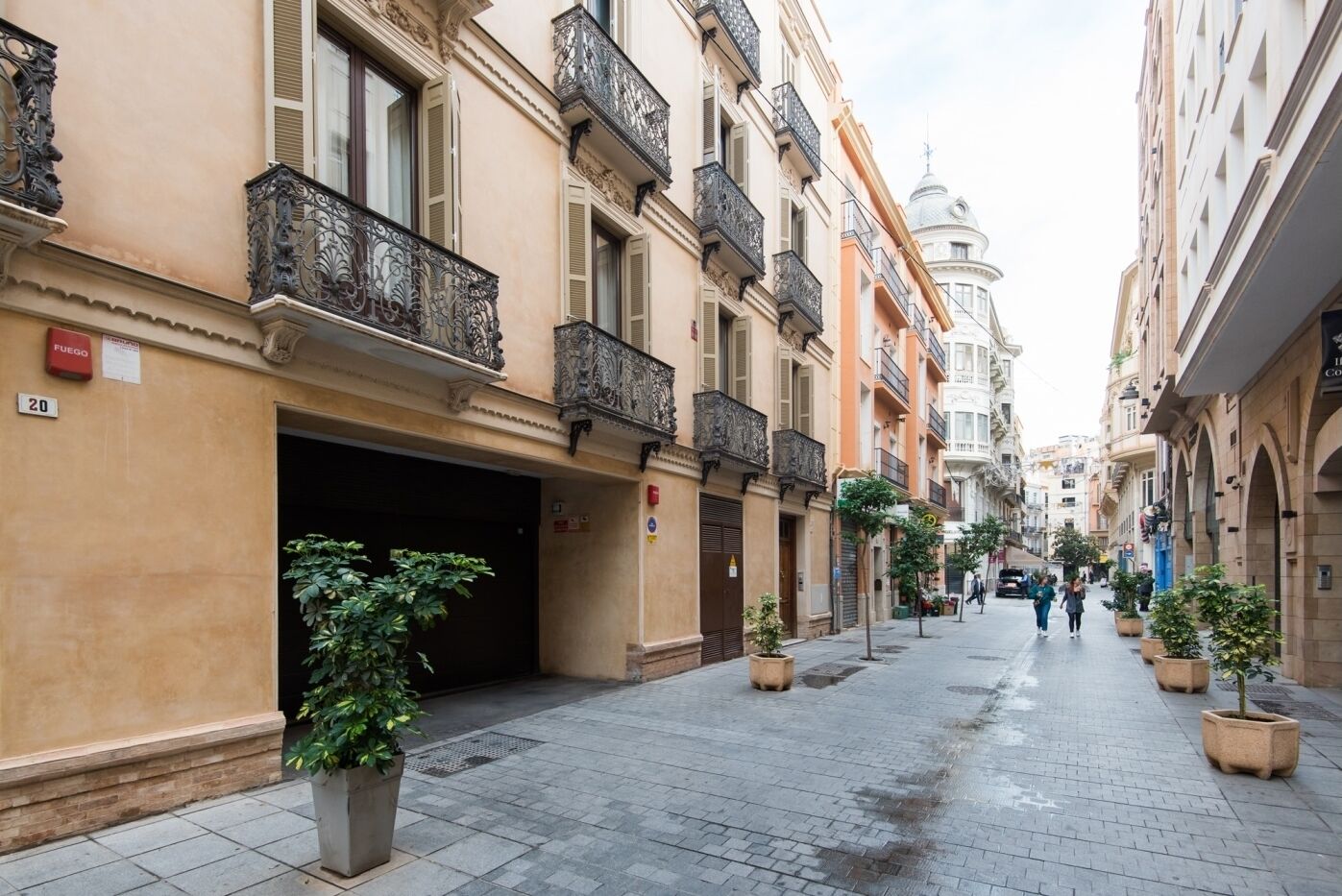 A narrow street lined with historic buildings, featuring balconies and a dome in the background.