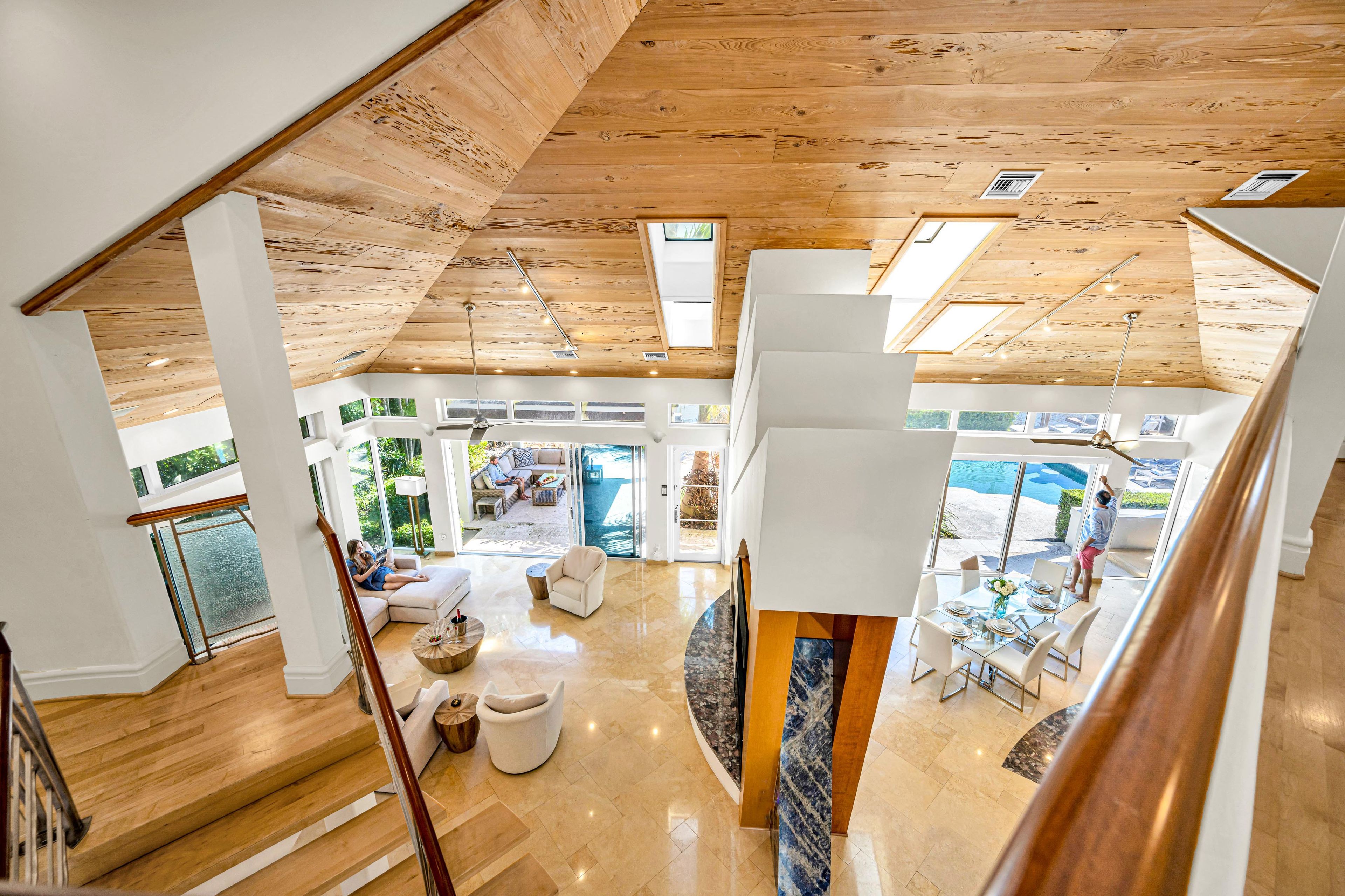 A spacious interior with a high ceiling, wooden beams, and a view of an outdoor swimming pool.