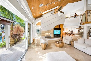 A spacious living area with a large TV, comfortable seating, and a view of the outdoors. - Architectural Masterpiece | Venice of America | Riverside View & Access | Nurmi Key | RESlDENCES (Fort Lauderdale)