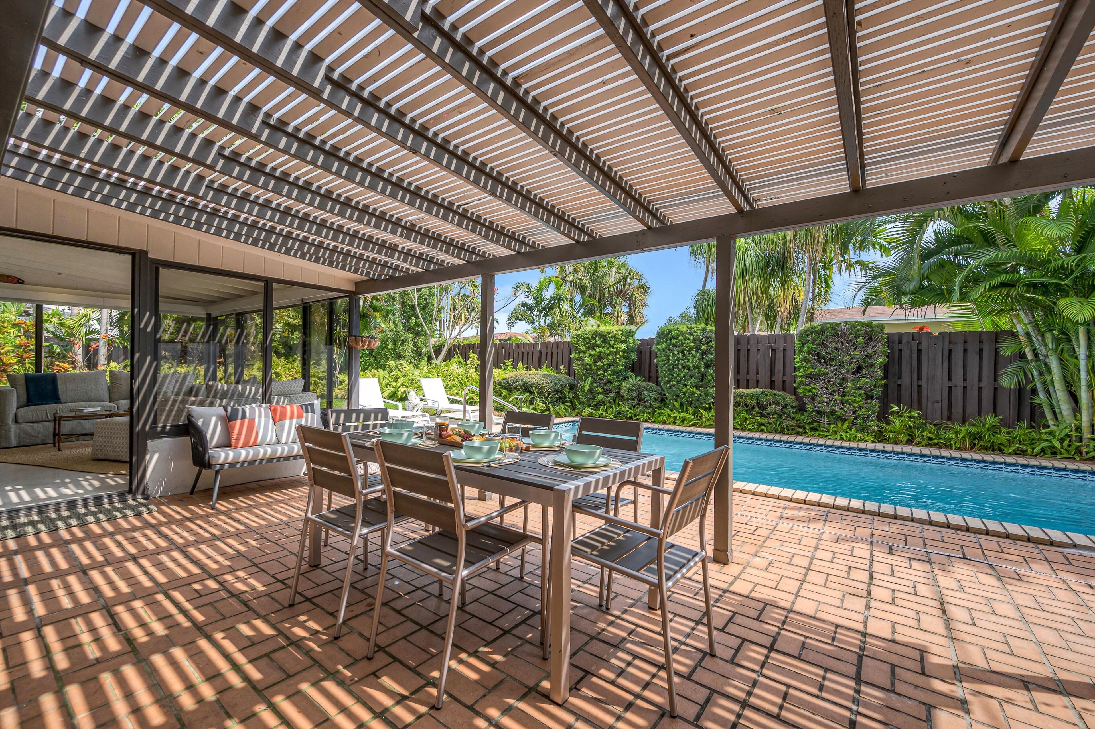 Une terrasse extérieure avec une piscine, un espace salon couvert et une table dressée pour les repas.