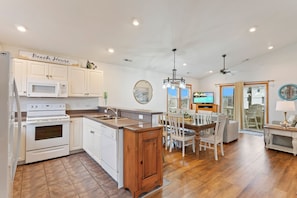 A spacious kitchen with white cabinets, a wooden island, and a dining area with white chairs.