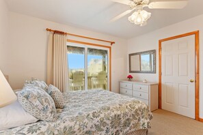 A bedroom with a bed, a dresser, a mirror, and a sliding glass door to a balcony.