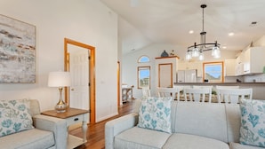 A spacious living room with a grey sofa set, a wooden side table with a lamp, and a large abstract painting on the wall. - 5180 Perfect Pastime * 5 Min Walk to Beach (Kill Devil Hills)