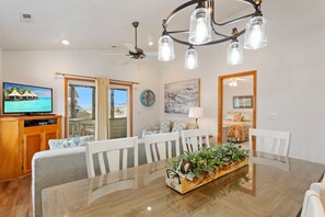 A dining area with a wooden table, white chairs, a chandelier, and a television on a wooden cabinet.