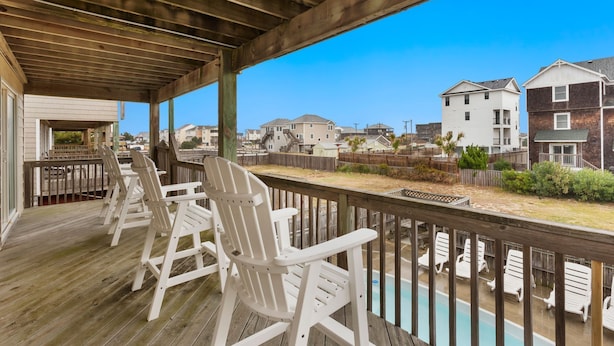 A wooden deck with white Adirondack chairs, a pool, and a view of residential buildings. - 5180 Perfect Pastime * 5 Min Walk to Beach (Kill Devil Hills)