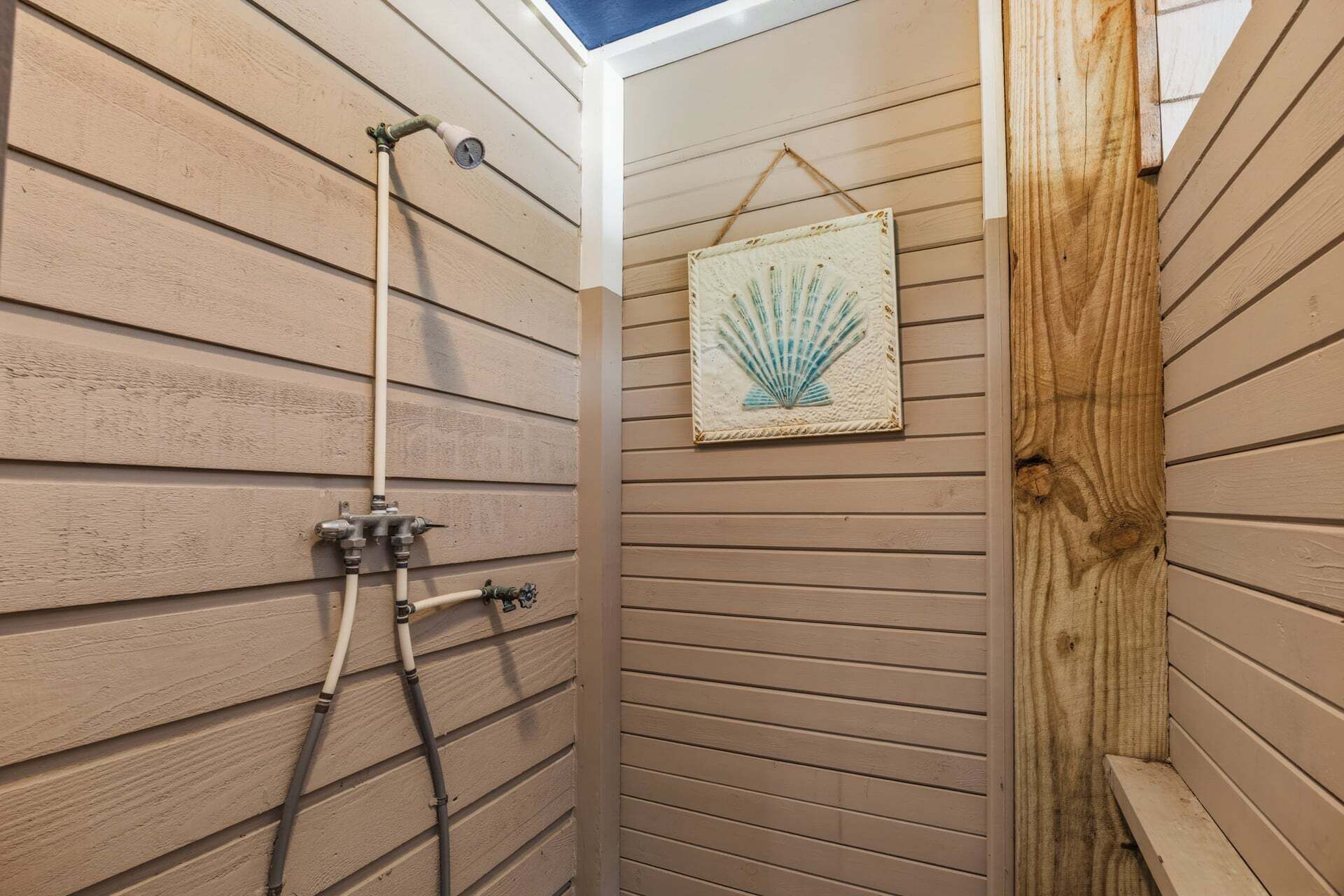 A corner shower with wooden paneling, a mounted thermometer, and a framed seashore artwork.