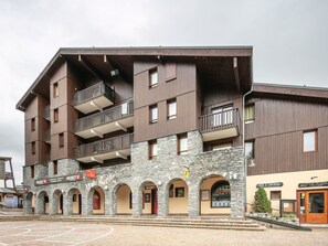 Ein mehrstöckiges Gebäude mit Balkonen, steinernen Bögen und Hinweisschildern für ein Skigebiet.
