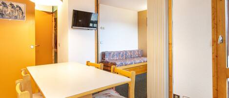 A room with a wooden table, chairs, a sofa, a television, and a sliding door.