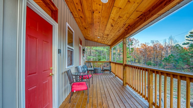 Une terrasse en bois avec une porte rouge, des sièges d’extérieur et une vue sur les arbres.