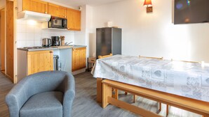 A compact kitchen with wooden cabinets, a microwave, a refrigerator, and a dining table with a patterned tablecloth. - Bright apt 4/6 ppl with balcony, near the ski runs (Saint-Sorlin-d´Arves)