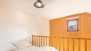 A bedroom with a wooden ceiling, a bed with white bedding, a small window with a view, and a wooden railing. - Bright apt 4/6 ppl with balcony, near the ski runs (Saint-Sorlin-d´Arves)