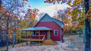 Una cabana de fusta vermella amb un porxo, envoltada per arbres d'autumn.