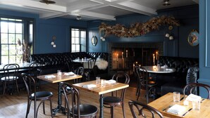 Un restaurant avec des tables en bois et des sièges en cuir noir, une cheminée et des éléments décoratifs sur les murs.