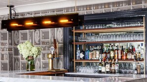 Un espace bar doté d’un comptoir en marbre, de tabourets et d’étagères remplies de bouteilles et de verres.
