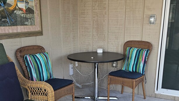 Un canapé en osier avec un coussin vert, deux fauteuils en osier avec des coussins à rayures et une petite table ronde sur laquelle se trouve un objet blanc.