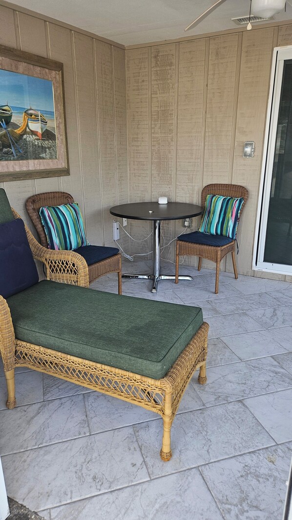 A wicker sofa with a green cushion, two wicker chairs with striped cushions, and a small round table with a white object on it.