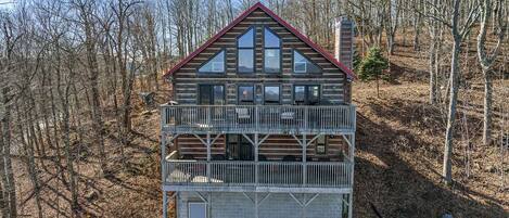 A two-story log cabin with a balcony, surrounded by a forest.