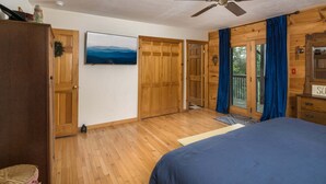 Ein Schlafzimmer mit einem Bett, einem Holzschrank, einem Deckenventilator, einem Fernseher und Blick durch eine Glastür.