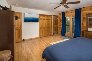 Ein Schlafzimmer mit einem Bett, einem Holzschrank, einem Deckenventilator, einem Fernseher und Blick durch eine Glastür.