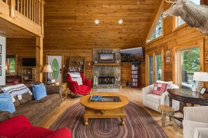 Ein gemütliches Holzblockhaus-Interieur mit Kamin, Holzmöbeln und einem aufgehängten Hirschkopf.
