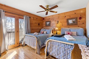 A cozy cabin room with two beds, a ceiling fan, and a large window.