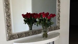 A mirror with an ornate frame on a white wall, above a white console table with a vase of red roses. - Golf Course Condo. X-Large 2 Bedroom (Rancho Mirage)