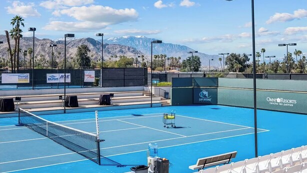 A tennis court with a net, surrounded by a fence, with a mountain backdrop and palm trees. - Golf Course Condo. X-Large 2 Bedroom (Rancho Mirage)