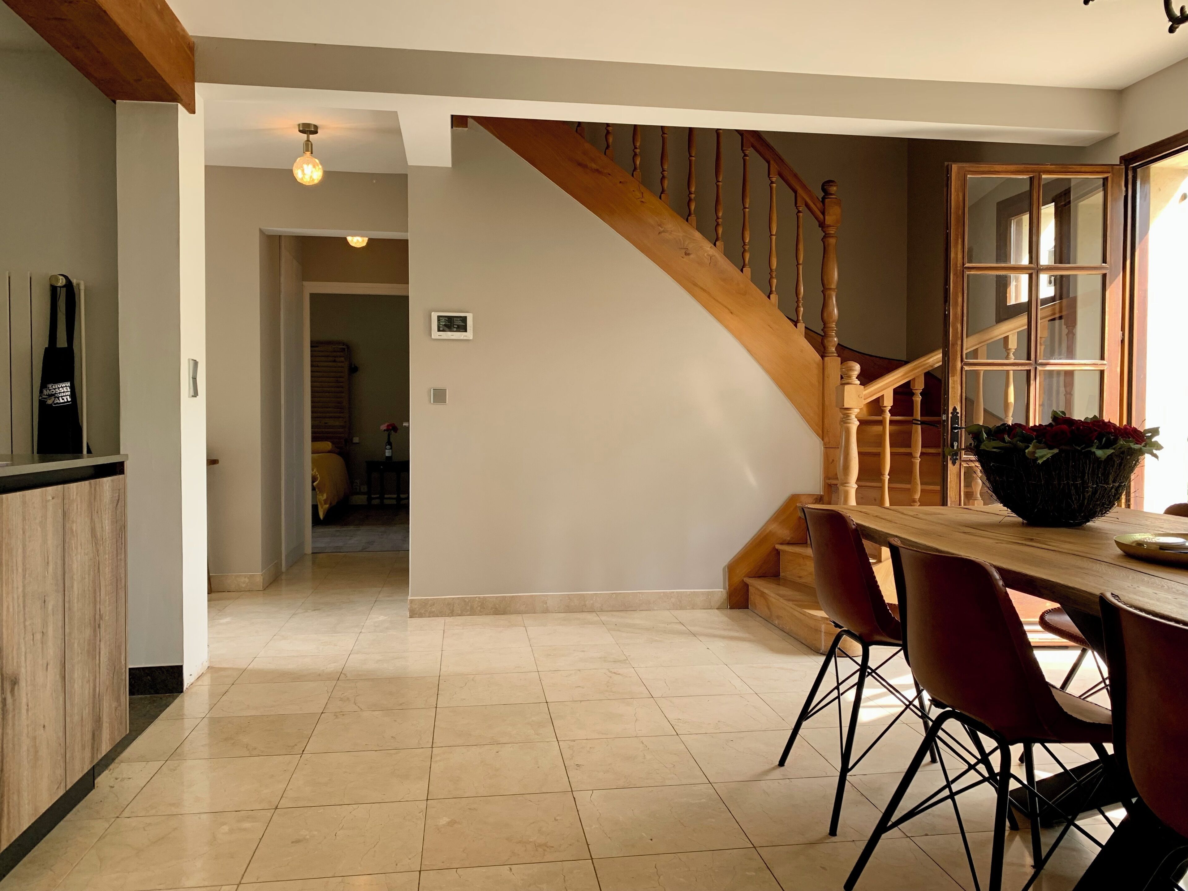 Una cocina moderna con una escalera de madera, un comedor con sillas rojas y vistas hacia un dormitorio.