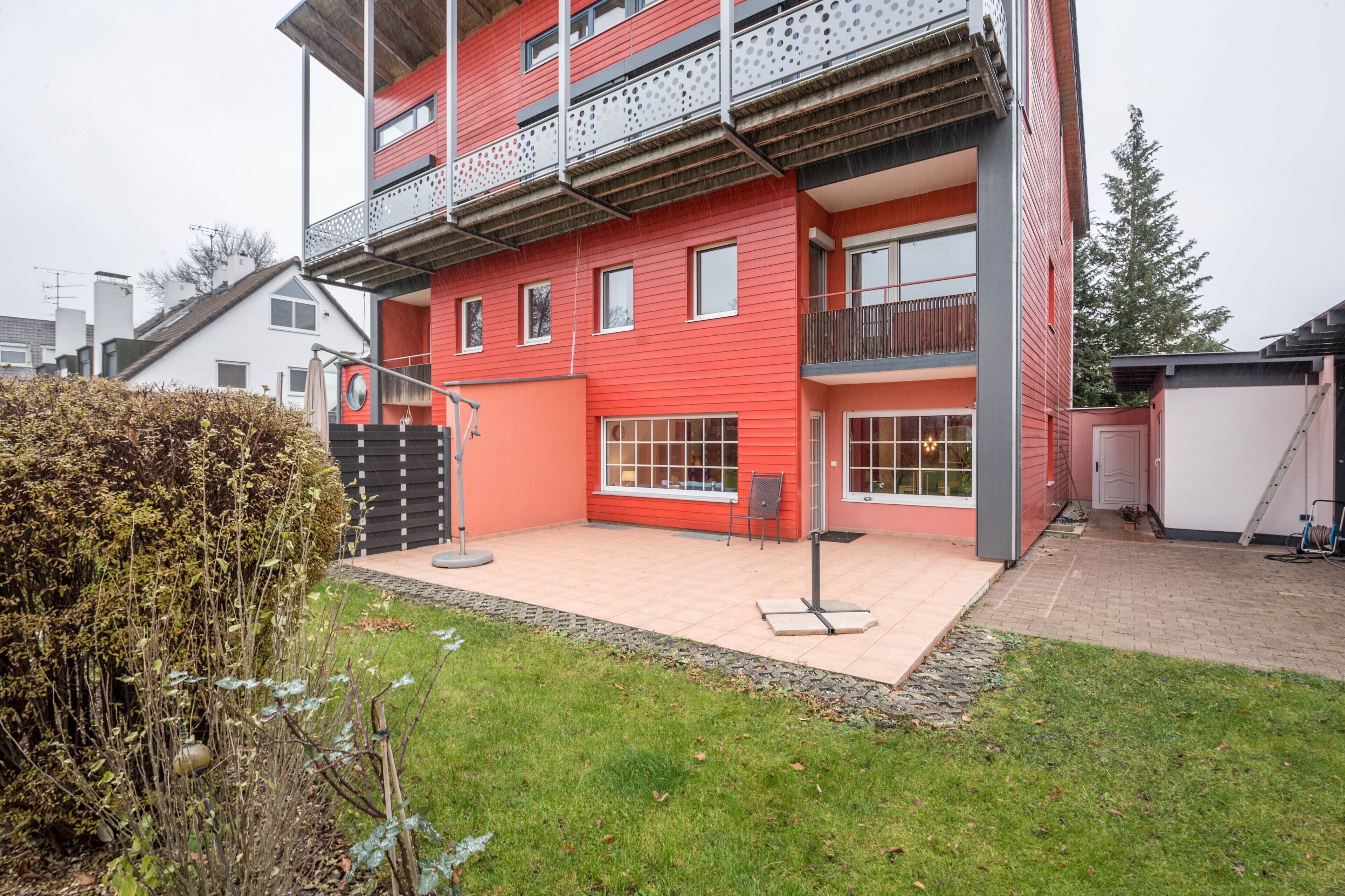 A multi-story building with a red facade, balconies, and a small patio area.