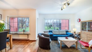 Un salon avec un canapé bleu, une table basse en bois, un fauteuil rouge et une table à manger avec des chaises.