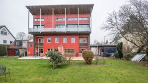 Un immeuble rouge à plusieurs étages, doté d’un balcon, d’un petit jardin et d’une clôture en métal.