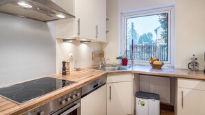 Une cuisine moderne équipée d’une cuisinière, d’un four et d’un évier intégrés, d’une fenêtre donnant sur des arbres et d’une petite poubelle.