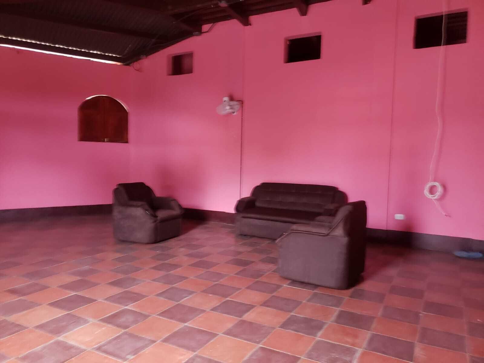 A room with pink walls, two black sofas, a small arched window, and a tiled floor.